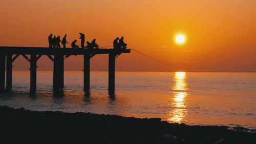 Silhouettes of Fishermen with Fishing Rods at Sea Sunset Sitting on the Pier. Slow Motion.
