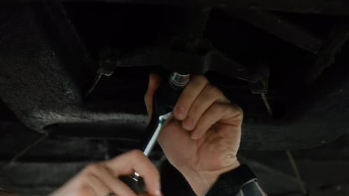 Car Service Mechanic Man Underneath Car Lifting Machine at the Garage