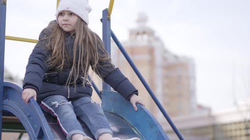 Niña alegre deslizándose por el tobogán en el patio de recreo. Cámara siguiendo a un niño caucásico divirtiéndose