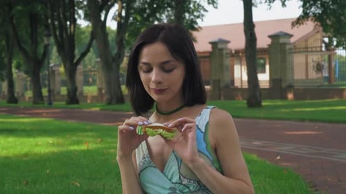 Attractive Brunette Girl Eating a Sandwich in the Park