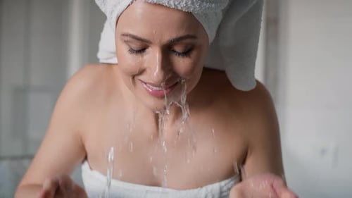 Vista frontal de la mujer lavándose la cara con agua en el baño. Tomada con cámara de helio RED en 8K.