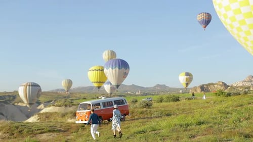 Couple Walking on Grassy Hill with Hot Air Balloons