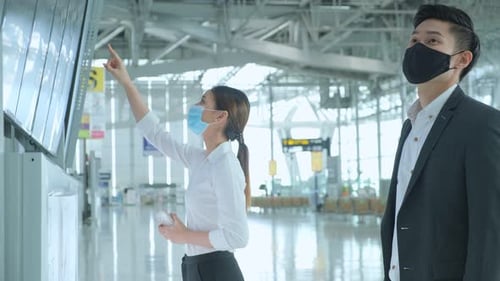 Man and Woman at Airport Flight Display Using Phones