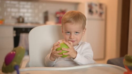 Blond Child Bites Into Green Apple in Kitchen