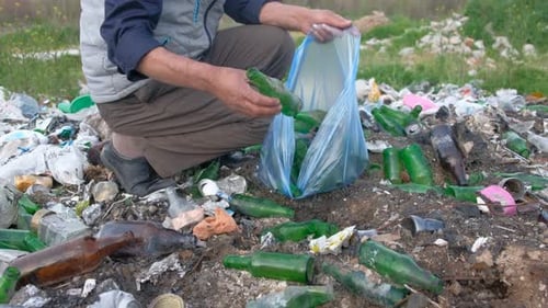 Man Picking Up Glass Bottles in Rural Trash Area