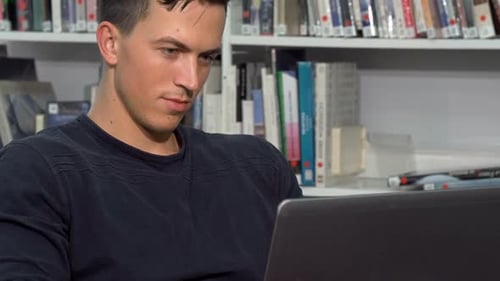 Étudiant attrayant travaillant sur un ordinateur portable à la bibliothèque du campus