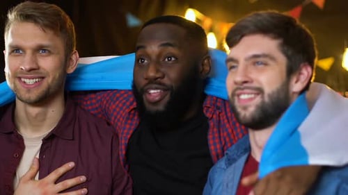 Friends Hugging and Cheering with Flag Indoors at Night