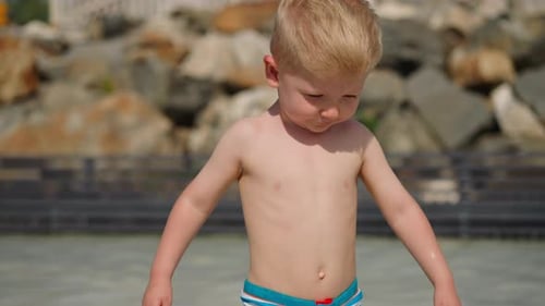 Adorable Little Boy in Shorts Walks Along Shallow Sea Water