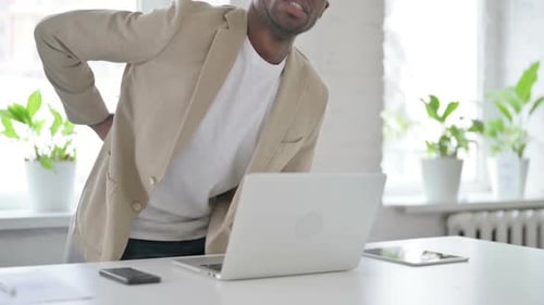African Man Having Back Pain While Using Laptop in Office