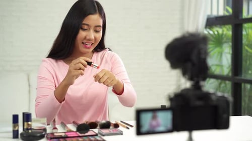 La bloguera de belleza presenta cosméticos de belleza mientras está sentada frente a la cámara frontal para grabar un vídeo.