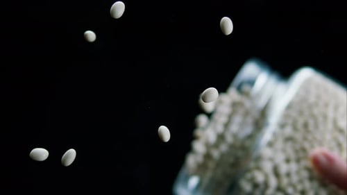 Closeup of Falling Down White Beans From Glass Jar on Black Background