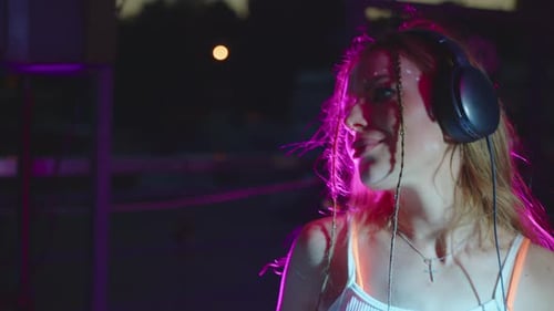 Woman with Headphones Dancing in Nightclub with Pink Lights