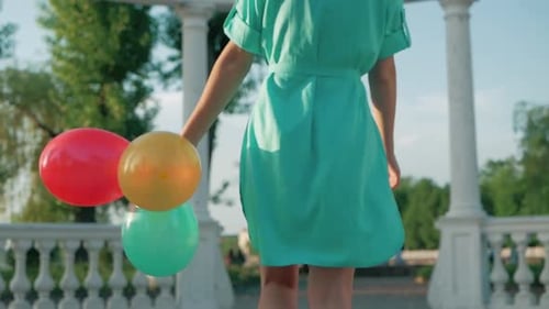 Young Woman in Green Dress Walks With Balloons