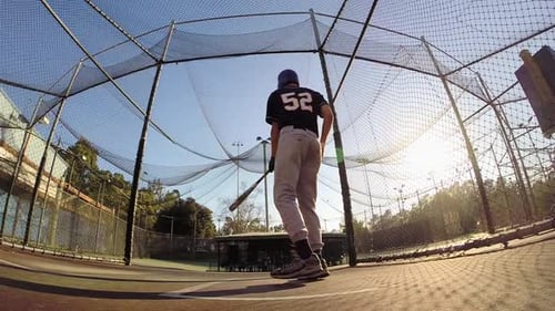 A baseball player practicing at the batting cages.