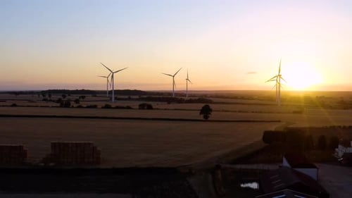 Large wind turbines with blades in field aerial view bright orange sunset.