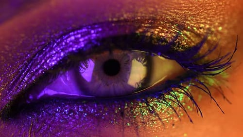 Primer plano extremo del iris del ojo humano bajo una luz de neón violeta. Mujer con hermoso maquillaje, purpurina