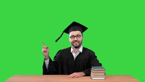 Young Graduated Man at the Desk Pointing To the Sides Presenting Something on a Green Screen Chroma