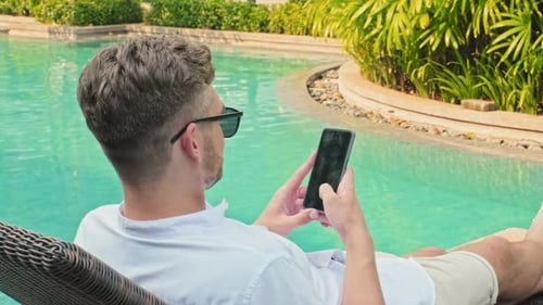 Man Using Smartphone by Pool at Luxury Tropical Resort