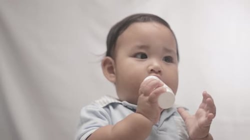 Cute Baby Boy Gnaws Plastic Bottle With White Background. - close up