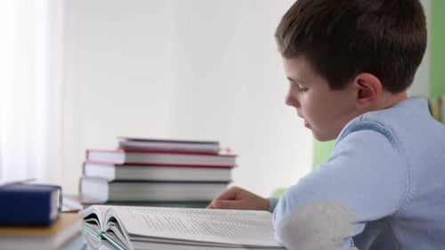 Boy Reads Aloud from Book at Table