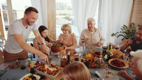 Man Cutting Roasted Turkey for Family at Thanksgiving Dinner