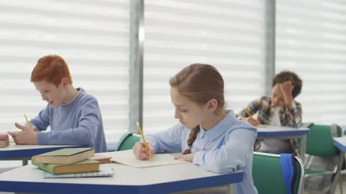 Students Writing at Desks in Bright Classroom