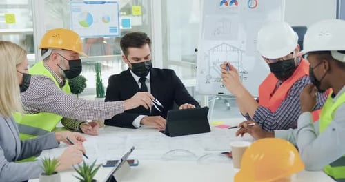Ingenieros enmascarados discuten detalles del edificio con un jefe seguro durante una reunión en la sala de juntas