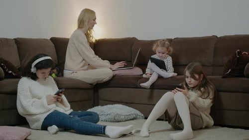 Mama arbeitet mit Laptop-Tochter mit Telefonen, während sie auf der Couch im Apartment Room Rbbro sitzt