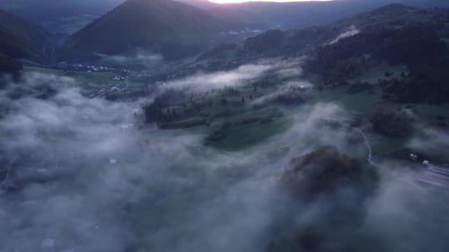 Luftaufnahme von Nebel im Tal mit Wäldern, Wiesen und Häusern an der Straße