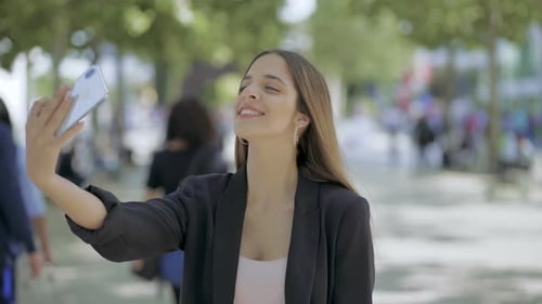 Smiling Woman Taking Selfie with Smartphone in Park