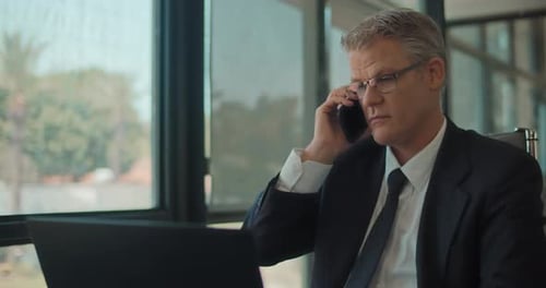 Businessman in formal wear and glasses talking on the phone while working at the office