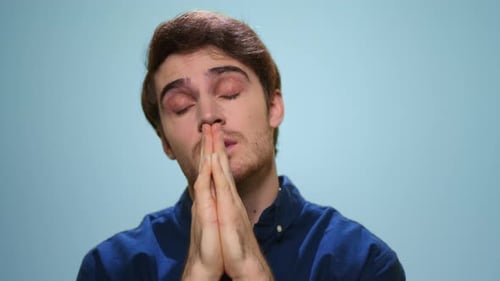 Konzentrierter Mann spricht Gebet im Studio. Hübscher Kerl betet auf blauem Hintergrund
