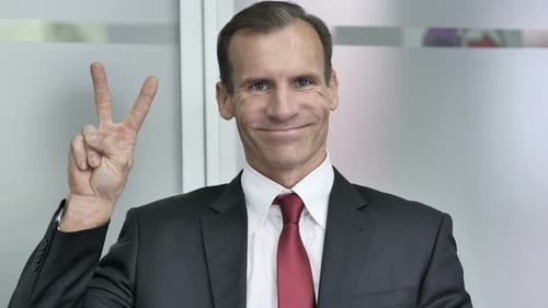 Smiling Businessman Showing Peace Sign in Office