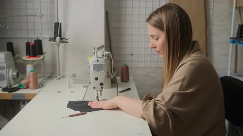 woman seamstress works at a sewing machine in workshop, enjoys the process. Fashion business