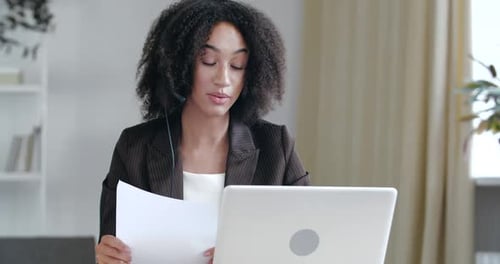 Curly American Tutor trägt drahtlose Kopfhörer, Unterricht in Online-Kursen, Verwenden von Papiernotizen