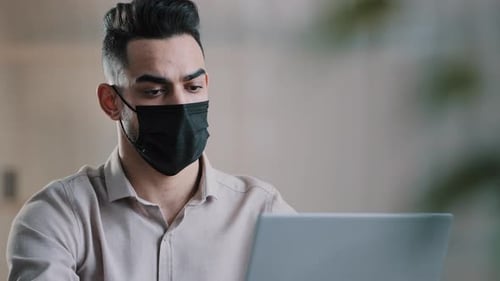 Man Wearing Face Mask Works at Laptop