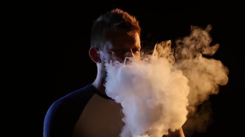 Man Vaping, Exhaling Cloud of Vapor in Dark Room Man Vaping, Exhaling Cloud of Vapor in Dark Room