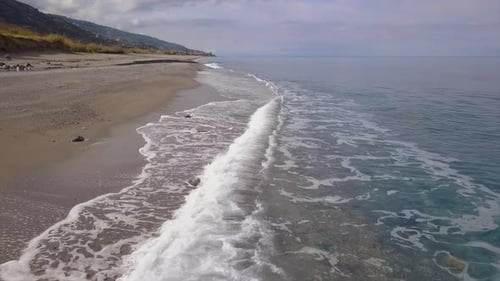 Drone flies over sea coast, aerial view of waves reaching shore and splashing breaking on beach