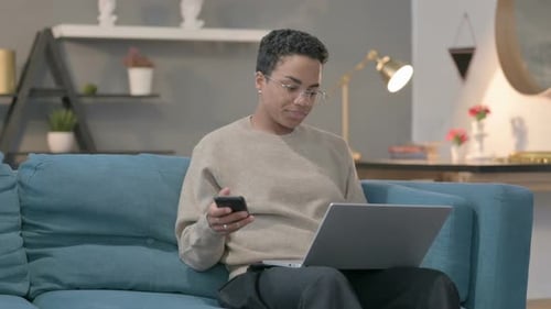 Young Adult Using Phone and Laptop on Couch