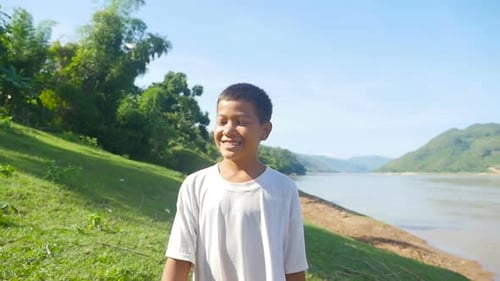 Menino andando e sorrindo perto do rio