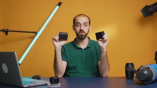 Man Presenting Camera Batteries at Desk in Studio