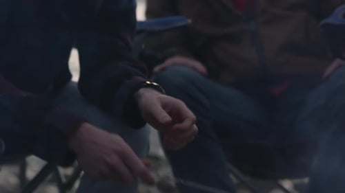 Hot dog roasting over campfire then pannng up to young men