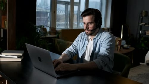 A young Man Uses a Laptop Works Online in a Cozy Dark Room at home in the Evening