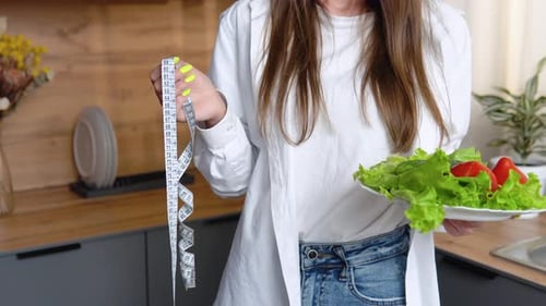 Woman Holds Salad and Measuring Tape in Kitchen