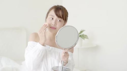 Woman Applying Makeup Looking into Mirror in Bedroom