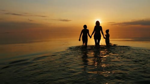 Mother with Two Children Go Swimming in the Sea at Sunset