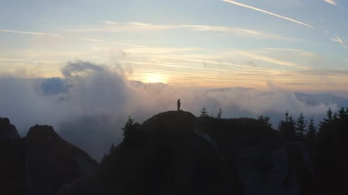 Person Standing on a Cliff Above the Clouds at Sunset
