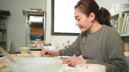 4K Asian woman enjoy painting self-made pottery plate at pottery workshop studio.