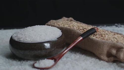 Raw Rice Grain In Unique Bowl, Rustic Bag And Wooden Spoon Rotate