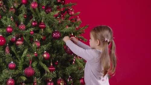 Girl Decorates Christmas Tree with Red Ornaments